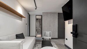 A modern room with a white sofa, a small round table, a chair, a built-in bench, a shower area, and a door with a handle. - Housy Laureles - 202 (Medellín)