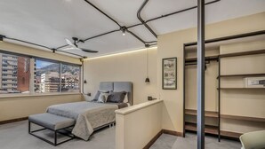A bedroom with a bed, bench, and a view of buildings through a large window. - Nutibara Express - 827 (Medellín)