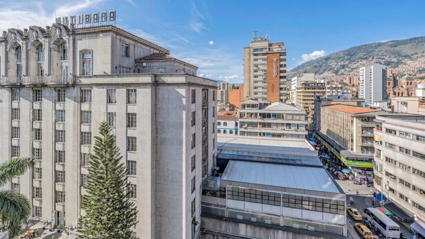 A multi-story building with a prominent sign, a modern glass structure, and a busy street with vehicles and pedestrians. - Nutibara Express - 827 (Medellín)