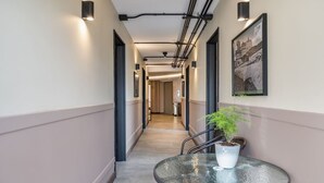 A hallway with a round table and potted plant, a framed picture on the wall, and exposed ceiling pipes. - Nutibara Express - 827 (Medellín)