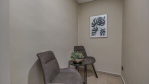 Una habitación de esquina con dos sillones grises, una mesita con una planta y una obra de arte enmarcada en la pared.