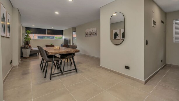 Un comedor con una mesa y sillas de madera, un espejo grande en la pared y una planta en maceta.