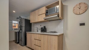 Cocina compacta con armarios de madera, microondas, cafetera y un reloj en la pared.