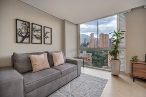 Een moderne woonkamer met een grijze bank, een groot raam met stadszicht en een potplant.