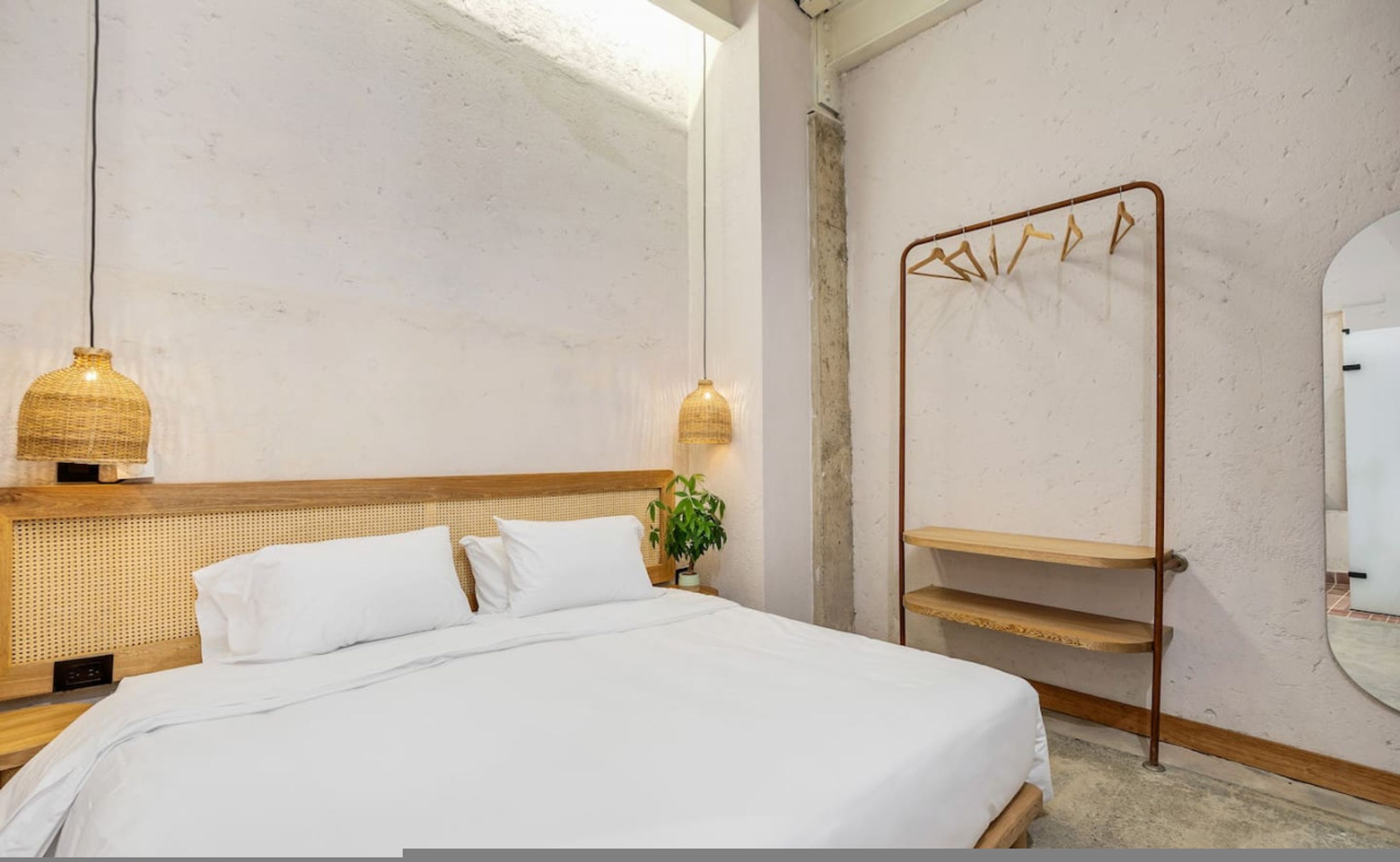 A bedroom with a bed, bedside lamps, a hanging rack, and a mirror.
