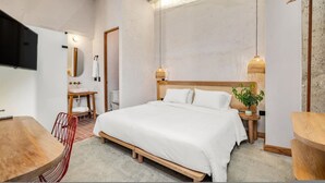 Un dormitorio con cama, mesita de noche, lámpara y televisión montada en la pared.