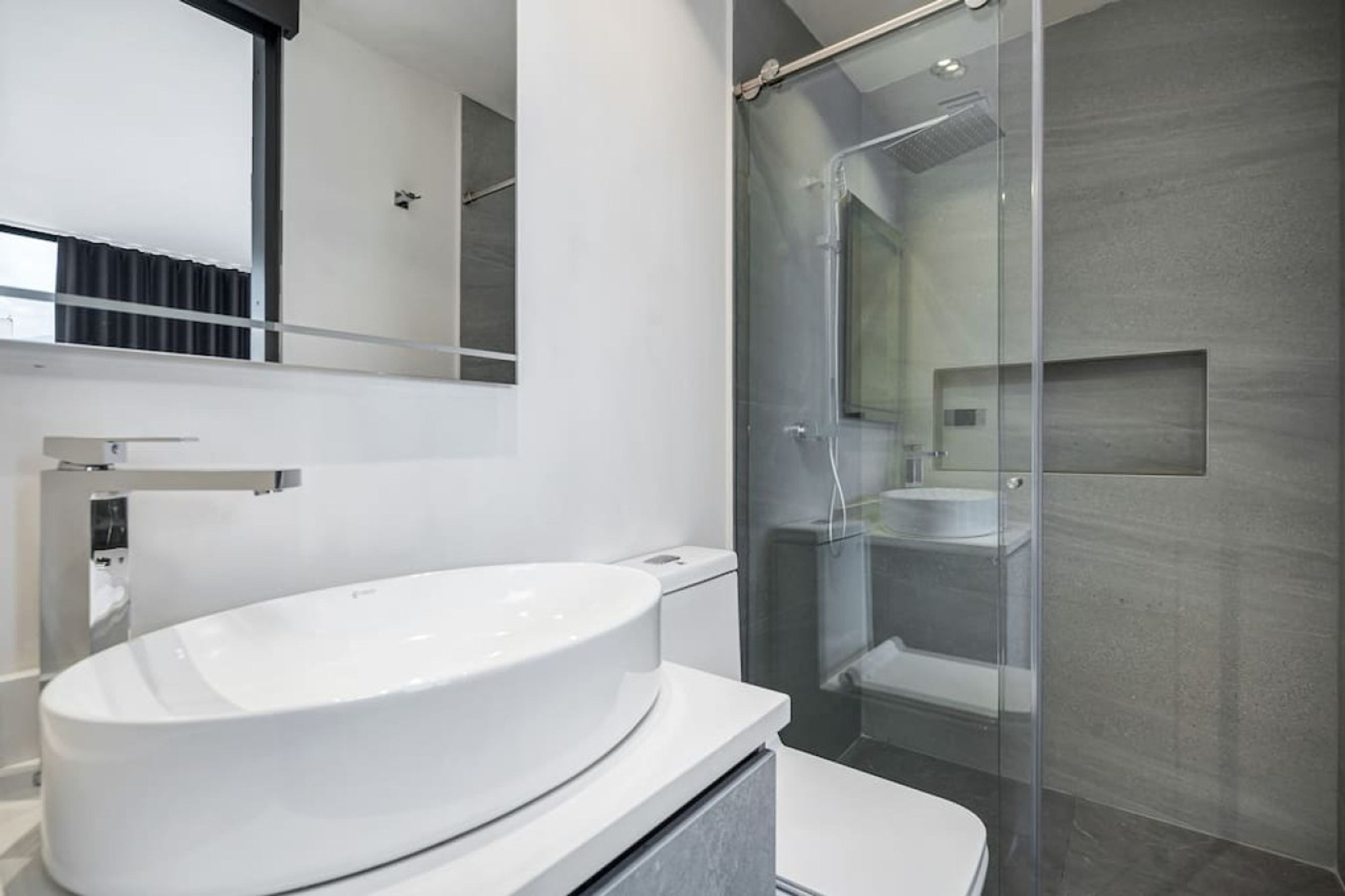 A modern bathroom with a large white sink, a glass shower enclosure, and a mirrored wall.