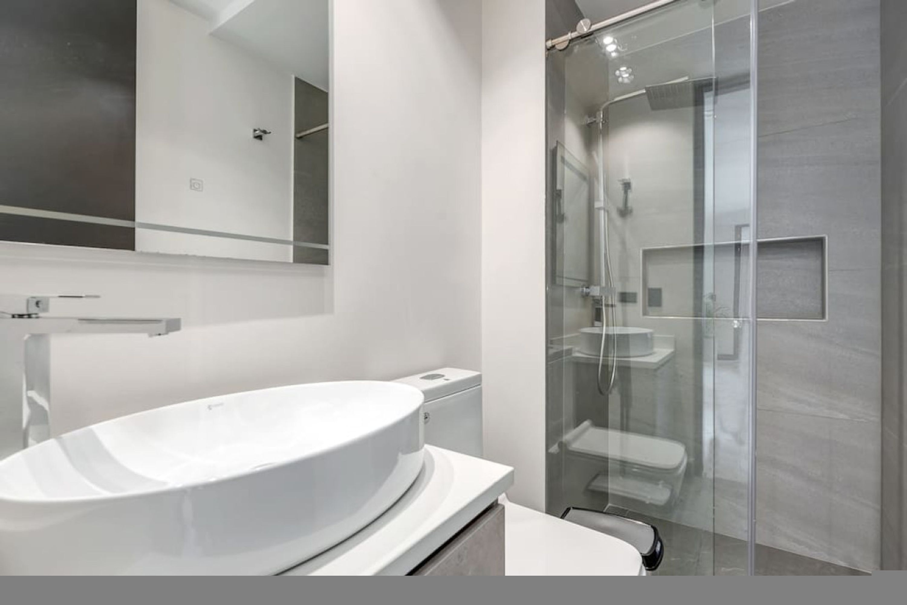 A modern bathroom with a large white sink, a glass shower enclosure, and a mirror above the sink.