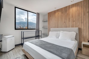 A modern hotel room with a large bed, a view of the city, and a wooden accent wall. - Housy Laureles - 302 (Medellín)