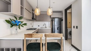 Eine moderne Küche mit weißer Arbeitsplatte, zwei Holzstühlen, einer Vase mit Blumen und Pendelleuchten.