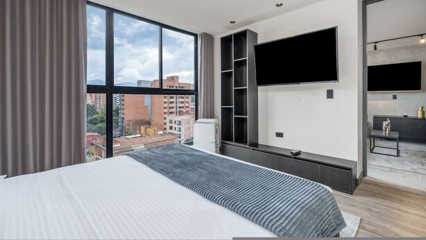 Ein modernes Hotelzimmer mit einem großen Bett, einem an der Wand montierten Fernseher und Blick auf die Stadt.
