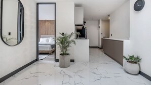 Een modern hotelinterieur met een marmeren vloer, een bed, een kitchenette en een grote spiegel.