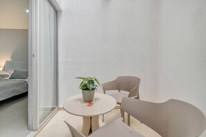 Quarto pequeno e moderno com cama, mesa e cadeiras, um vaso de planta e uma porta de vidro deslizante.