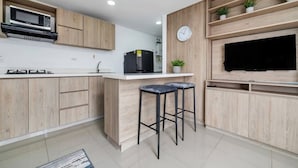 Une cuisine moderne avec des meubles en bois, un four à micro-ondes, un réfrigérateur, une horloge et un téléviseur fixé à un mur en bois.