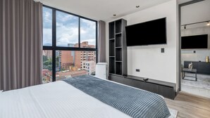 Ett modernt hotellrum med en stor säng, en tv som är monterad på väggen, en inbyggd garderob och utsikt över stadsbilden.