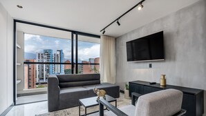 Ett modernt vardagsrum med en soffa, ett soffbord, en tv och utsikt över staden genom stora fönster.