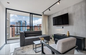A modern living room with a sofa, a coffee table, a TV, and a city view through large windows. - Housy Laureles - 701 (Medellín)
