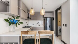 Ett modernt kök med en vit bänkskiva, två hänglampor, en vas med blommor och en tvättmaskin i bakgrunden.