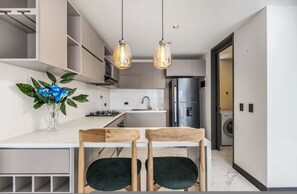 A modern kitchen with a white countertop, two pendant lights, a vase with flowers, and a washing machine in the background. - Housy Laureles - 701 (Medellín)
