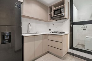 Eine kompakte Küche mit integriertem Mikrowellenherd, einem Edelstahl-Kühlschrank, einem Gasherd und einem Wasserspender.