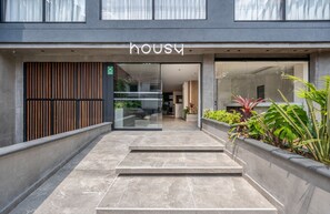 A modern building entrance with a 'HOUSE' sign, a glass door, and a concrete staircase leading inside. - Housy Laureles - 203 (Medellín)