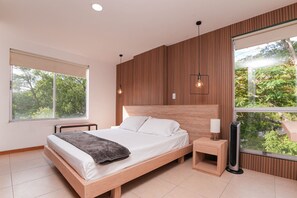 A modern bedroom with a wooden headboard, a large window with a view of trees, a bedside table with a lamp, and a standing heater. - Cyan 803 - 2BR in Medell n (Medellín)
