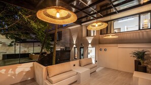 An indoor seating area with cushioned sofas, woven pendant lights, and a large window overlooking a tree. - Luxurious 5BR House in Provenza Perfect for Groups (Medellín)