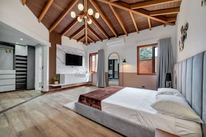 Un dormitorio con una cama grande, vigas de techo de madera, un televisor y un baño de diseño moderno.