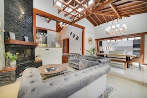 Una sala de estar moderna con chimenea, sofás grises, una zona de comedor y una cocina al fondo.