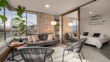 A modern room with a sofa, two chairs, a bed, a large window, and a brick wall.