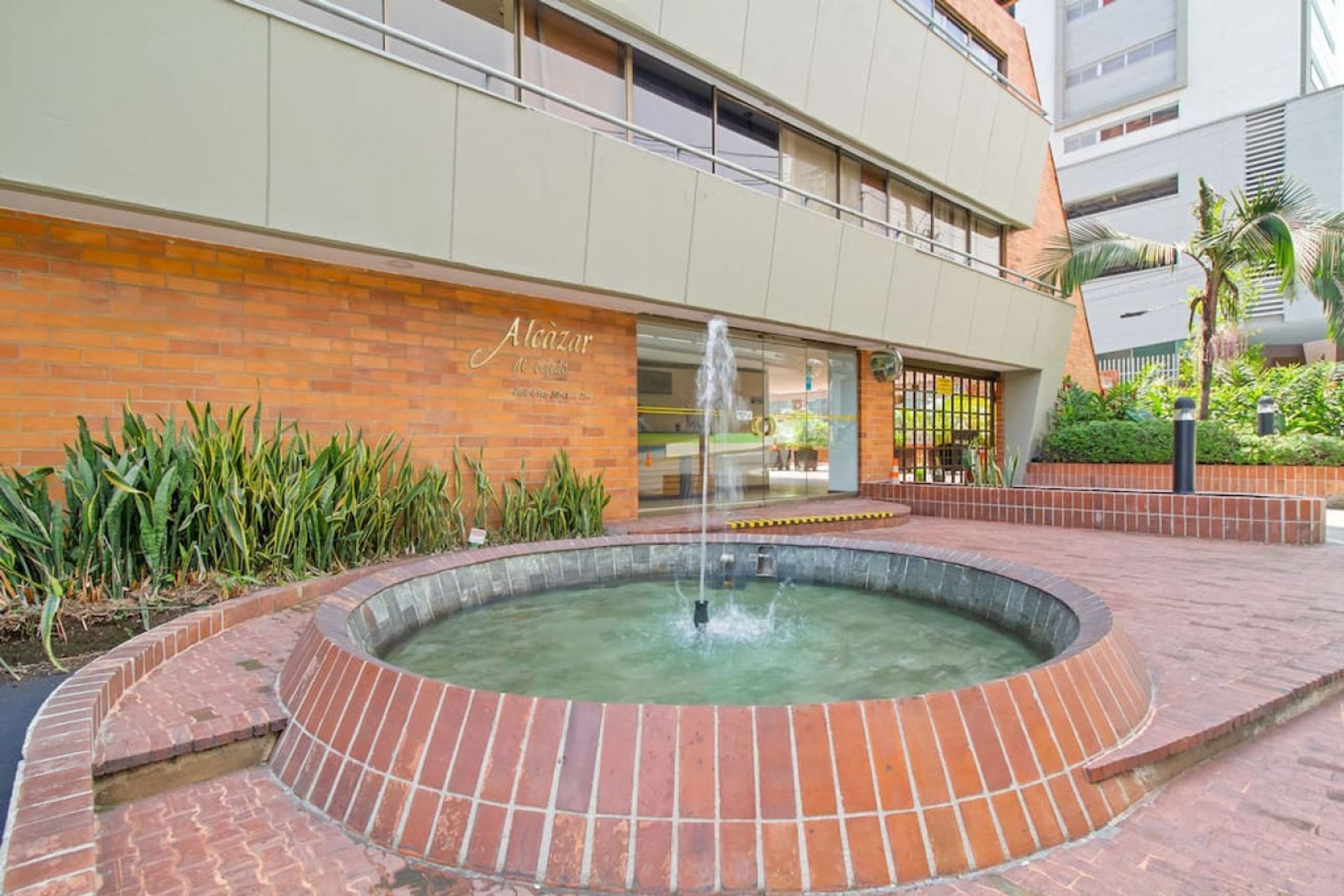 A courtyard with a brick fountain, a building with a sign reading 'Alaçazar de Córdova,' and a palm tree.