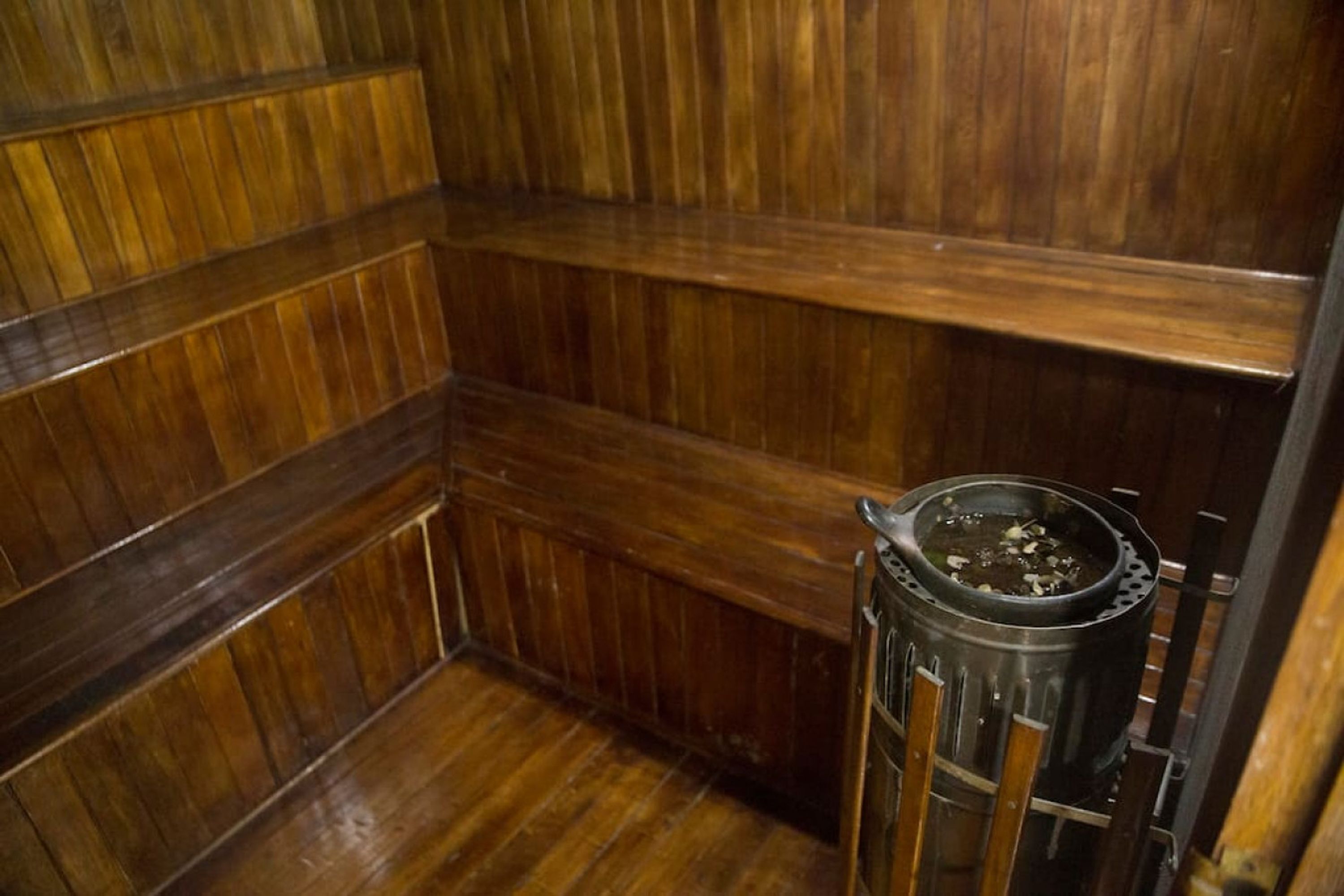 Una habitación con paneles de madera y un recipiente metálico sobre un pedestal.