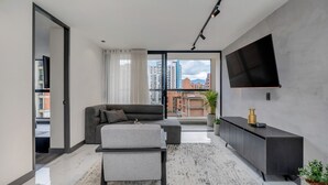 A modern living room with a sofa, ottoman, and a flat-screen TV mounted on the wall. - Housy Laureles - 601 (Medellín)