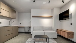 Una cocina moderna con armarios integrados, un rincón comedor con sofá y mesa, y un televisor montado en la pared.