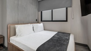 Una habitación de hotel moderna con una cama grande, un televisor de pantalla plana en la pared y una ventana con persianas.