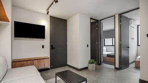 Una habitación de hotel moderna con una televisión de pantalla plana, un banco de madera, una mesita pequeña y una planta en maceta.