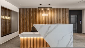 Un mostrador de recepción con encimera de mármol, listones de madera en la pared y un letrero que dice 'RECEPCIÓN'.