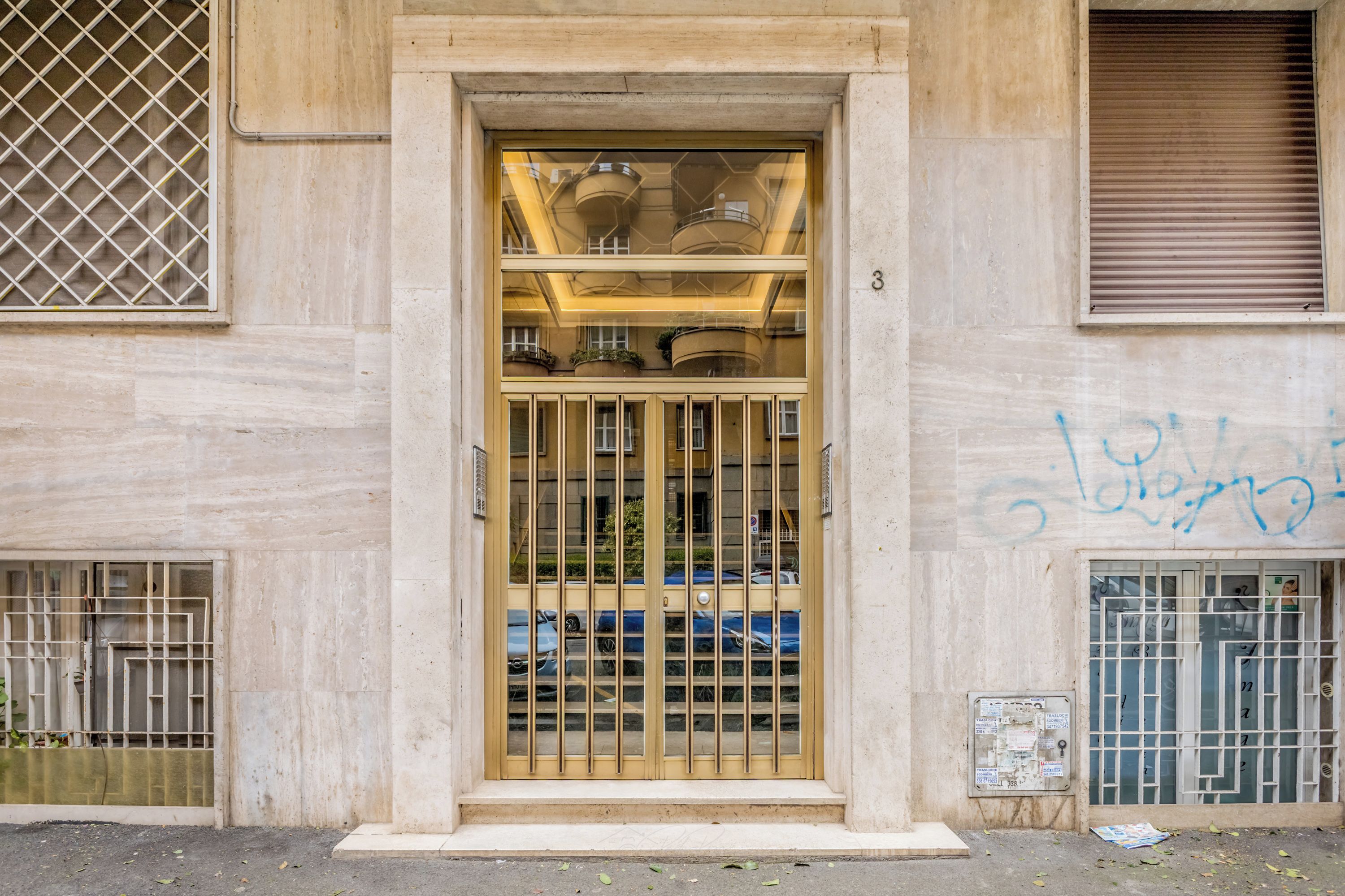Entrada de un edificio con una puerta de metal, unos pocos escalones y el número 3 sobre la puerta.