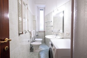 Casa de banho com sanita, bidé, lavatório e máquina de lavar roupa.