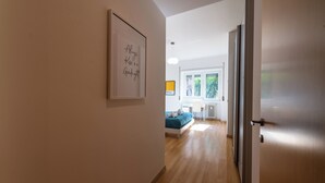 Un pasillo que lleva a un dormitorio con cama, escritorio y ventana con vistas a zonas verdes.