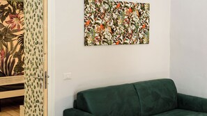 A room with a green sofa, a wall with a botanical print, and a partially visible door with a patterned curtain. - Vico Sedil Capuano 21 (Naples)