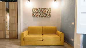 A room with a yellow sofa, a floral wall art piece, and a wooden door. - Vico Sedil Capuano 21 (Naples)