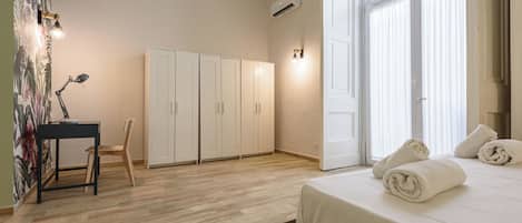 A bedroom with a bed, a desk with a chair, a wardrobe, and a door with curtains.