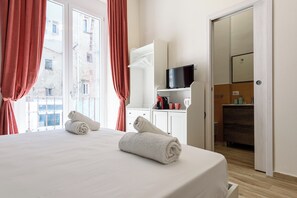 A hotel room with a bed, a television, a bathroom, and a view of buildings outside. - Vico Sedil Capuano 21 (Naples)