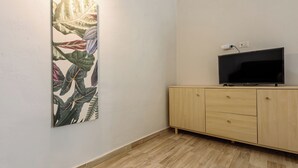 Una habitación con una televisión de pantalla plana sobre un mueble de madera, una obra de arte colgada en la pared y un interruptor de luz.