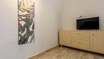 Una stanza con una TV a schermo piatto su un mobiletto in legno, un'opera d'arte appesa al muro e un interruttore della luce.