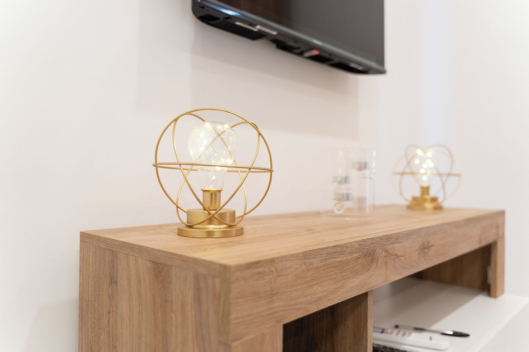 Une console en bois surmontée de deux lampes sphériques dotées d’un cadre en fil d’or et d’un abat-jour en verre.