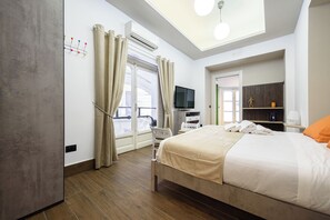 Ein Hotelzimmer mit einem Bett, einem Fernseher, einem Schreibtisch und einem Fenster mit Vorhängen.