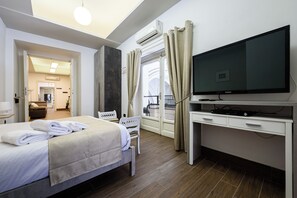 Ein Hotelzimmer mit Bett, Schreibtisch, Flachbildfernseher, Sessel und einem Fenster mit Vorhängen.