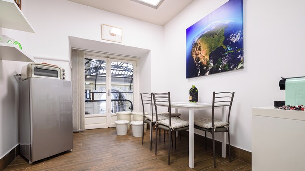 A kitchen with a refrigerator, a dining table with chairs, a window with curtains, and a large painting of Earth. - Piazza Nicola Amore 14 (Naples)